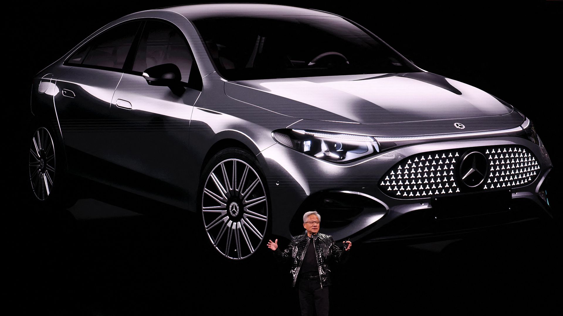 Nvidia CEO Jensen Huang, dressed all in black, stands before a giant screen depicting a Mercdes Benz vehicle at the CES technology show in Las Vegas.