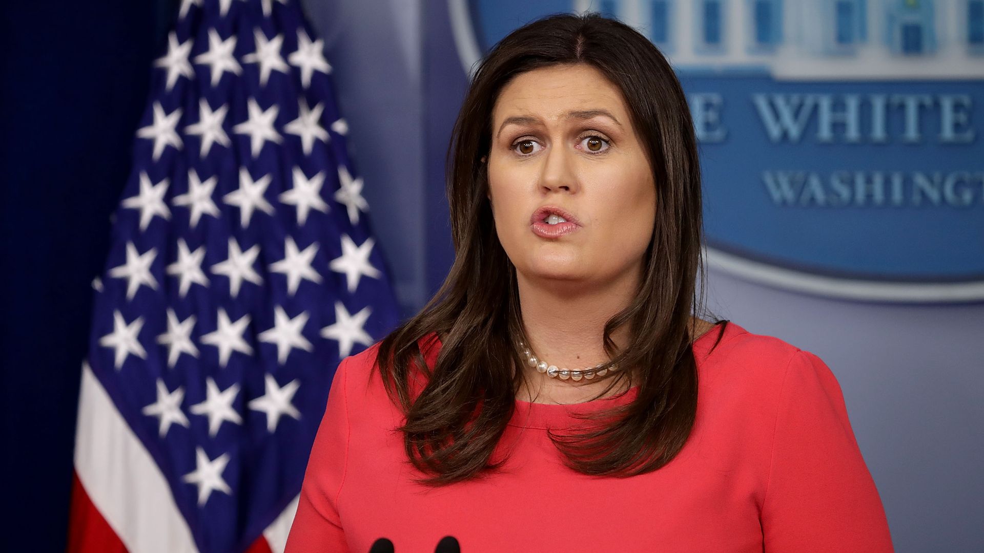 Sarah Sanders talking at the podium in a red suit