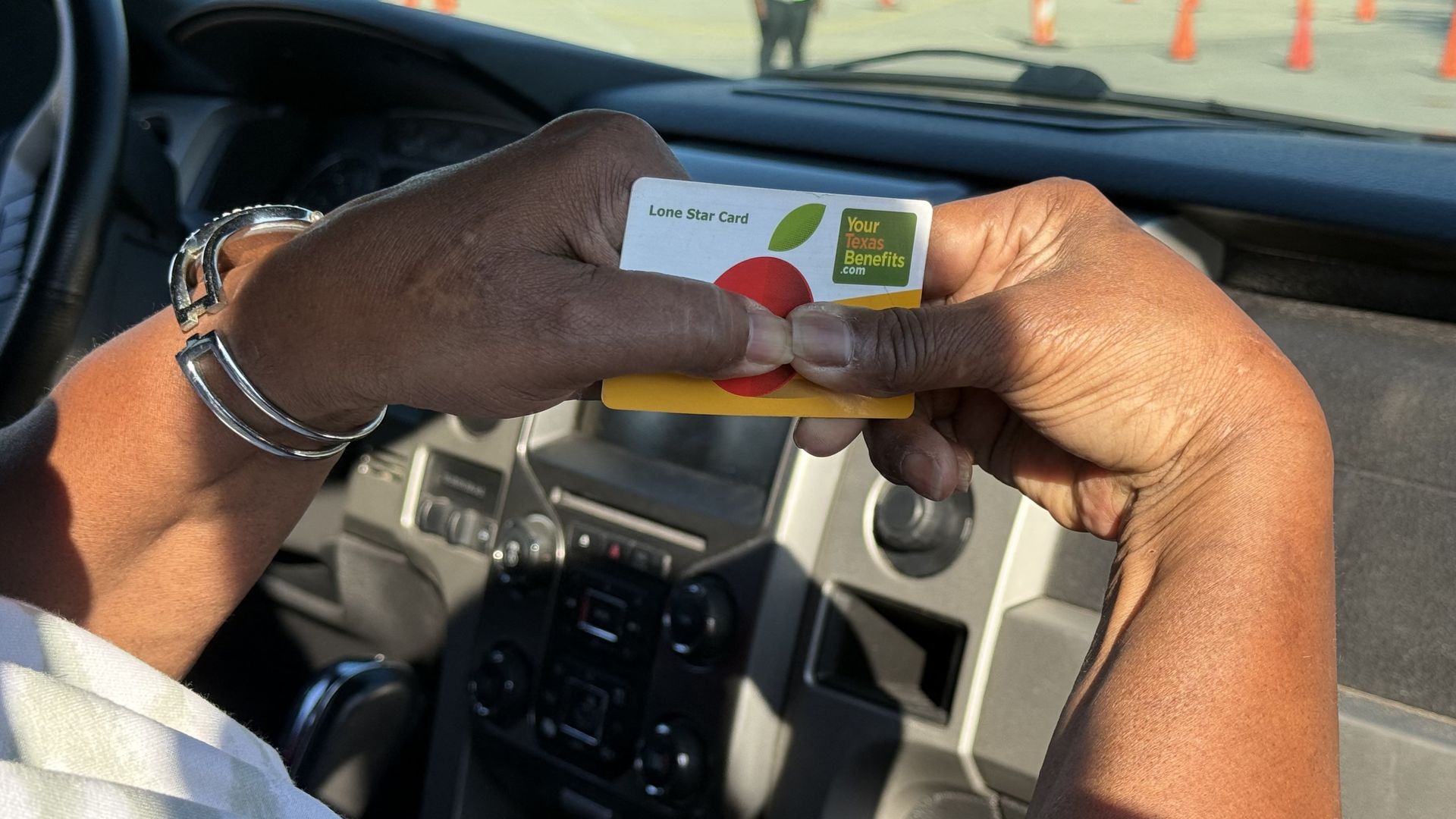 Person in a car holding a "Lone Star Card" that says "yourtexasbenefits.com" 