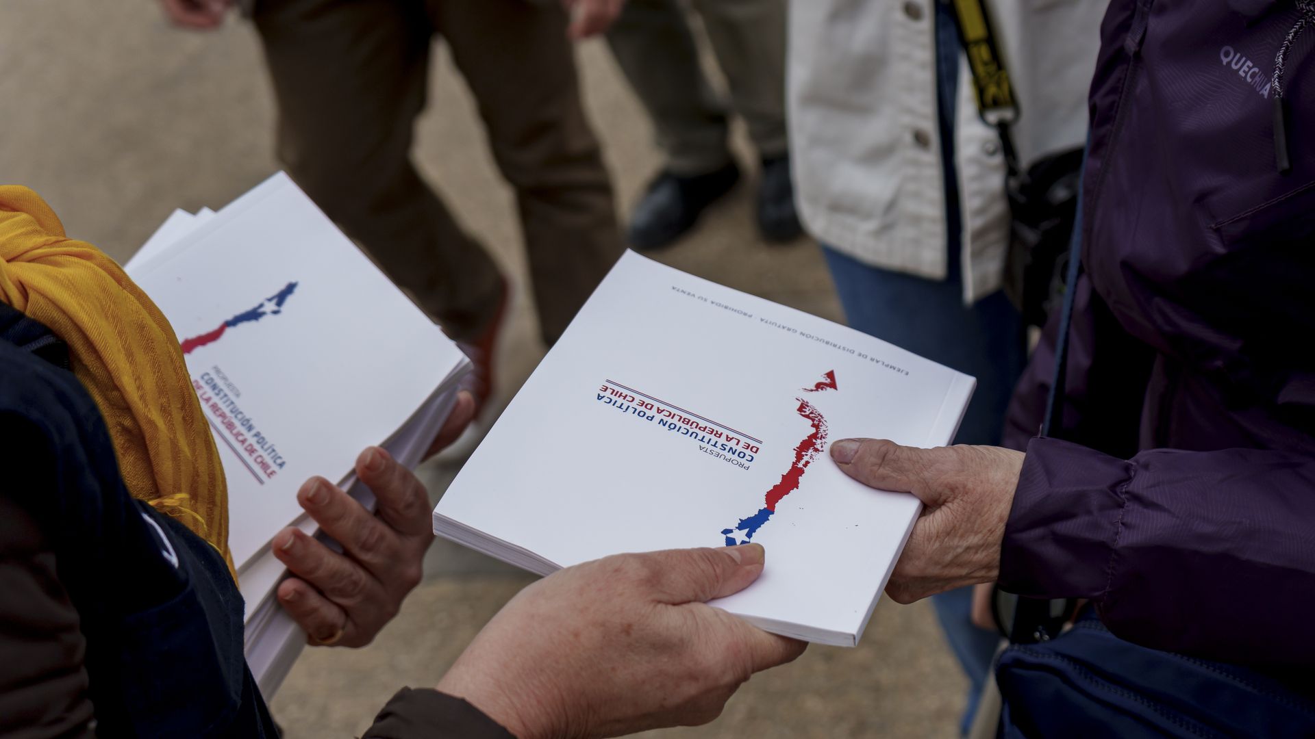 a person is handing over a draft of Chile's proposed new constitution to another person. their faces are not shown, just their hands