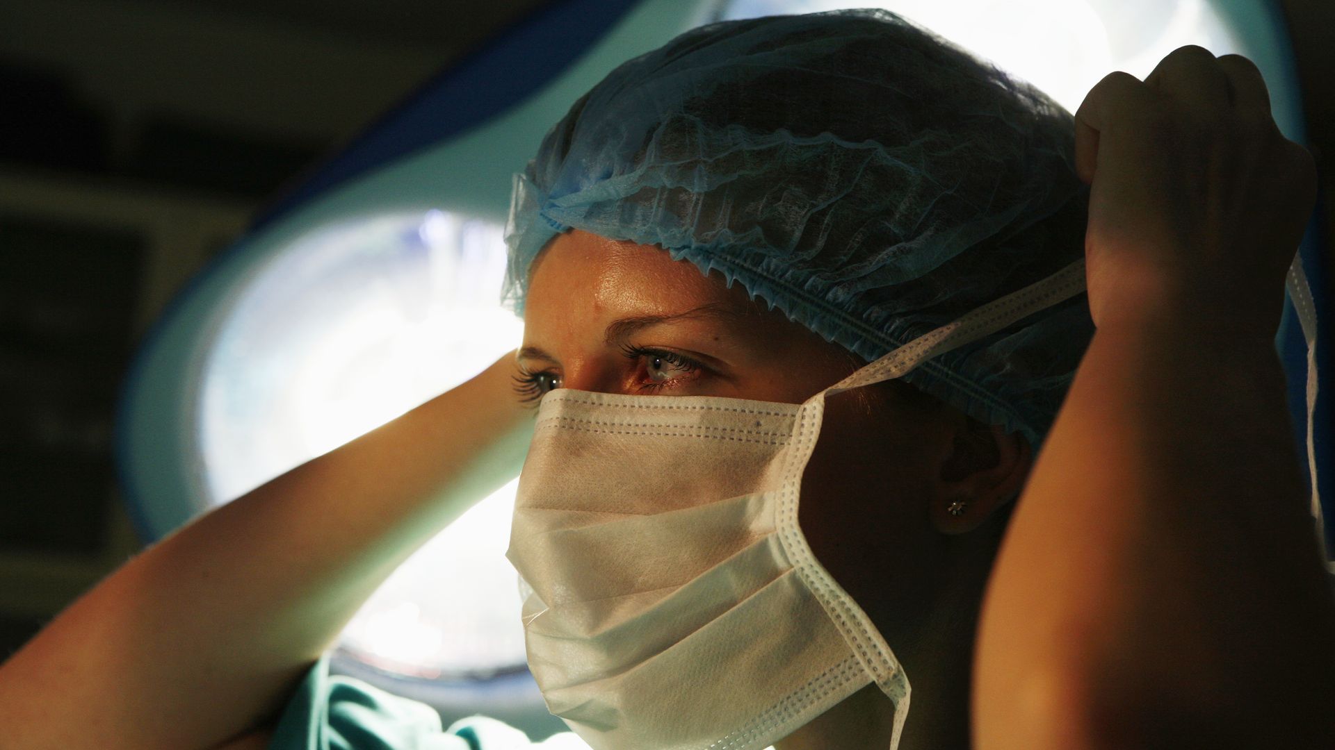 A female surgeon ties her surgical mask around her face.