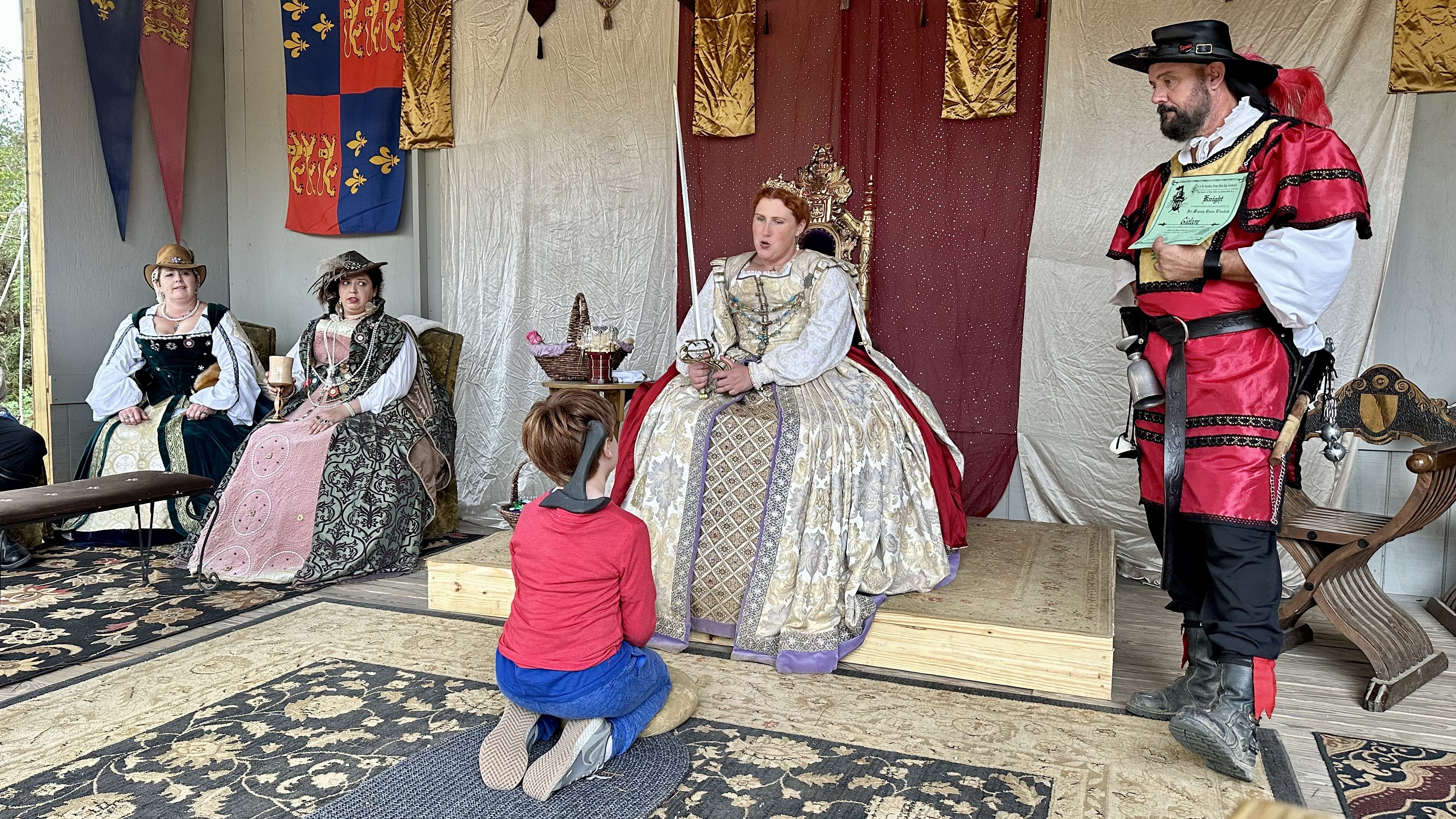 Photo shows a queen knighting a boy.