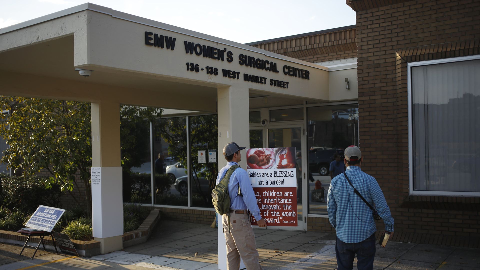 Picture of the entrance of an abortion clinic with people waiting outside holding anti-abortion signs
