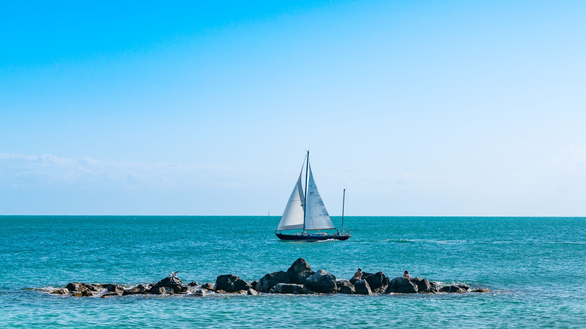 A sailboat with two full triangular sails in clear blue waters on a sunny day
