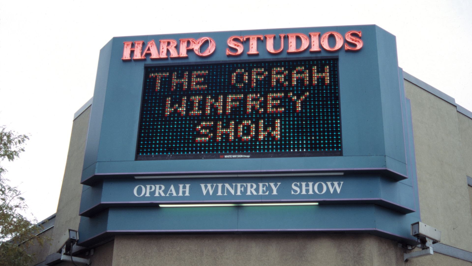 Blue Harpo Studios sign with red neon 'HARPO STUDIOS' above a digital marquee reading 'THE OPRAH WINFREY SHOW' and a blue panel below showing 'OPRAH WINFREY SHOW'.