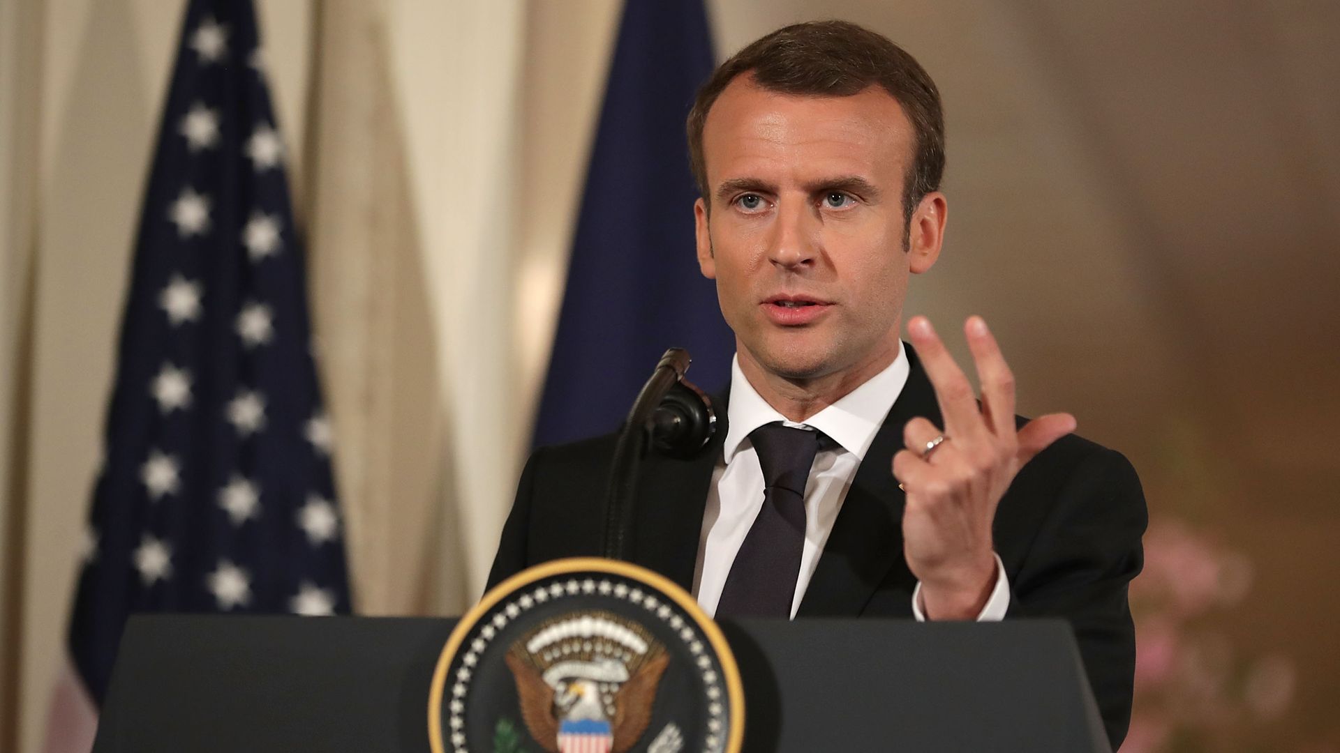 French President Emmanuel Macron speaking at White House lectern and making hand gesture