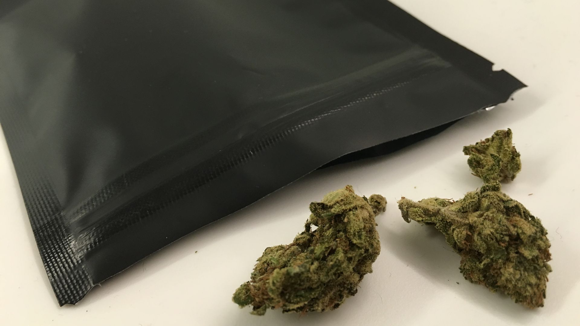 Marijuana buds coming out of a black plastic package