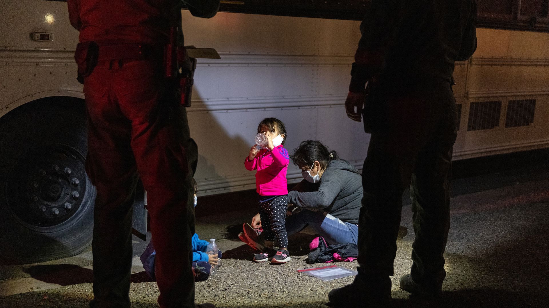 Picture of a migrant child standing in front of border patrol officers.