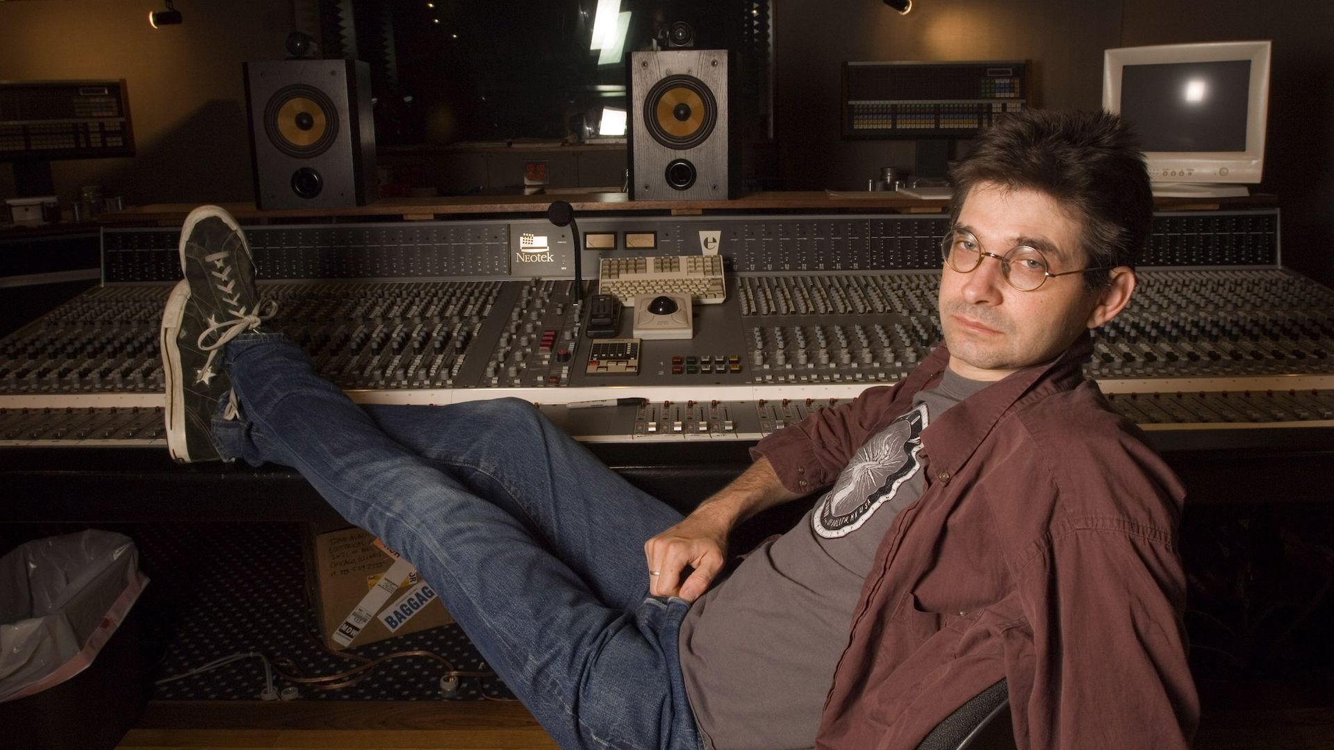 Steve Albini wearing jeans and button-down shirt with his feet up on a mixing board.