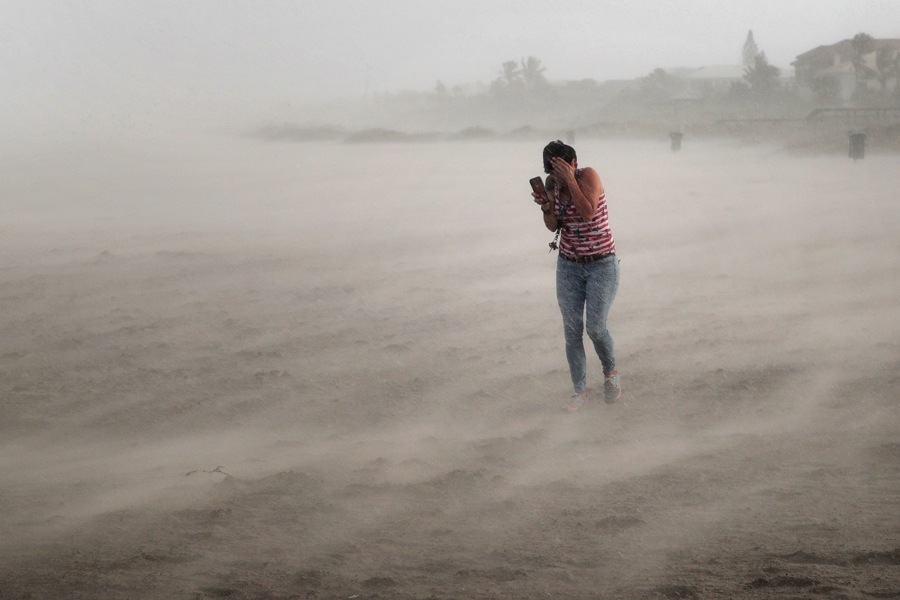 A woman seeks cover from wind, blowing sand and rain whipped up by Hurricane Dorian as she walks on the beach on September 2