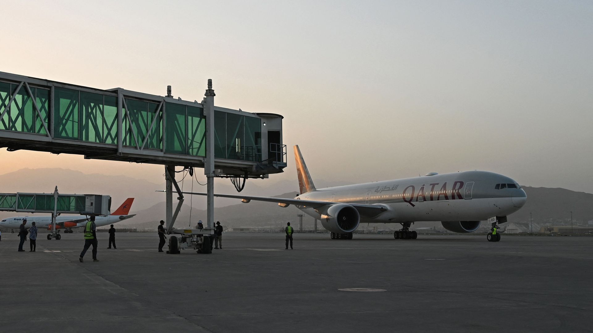 Members of ground staff stand on the tarmac as a Qatar Airways aircraft taxis before taking off from the airport in Kabul on September 9