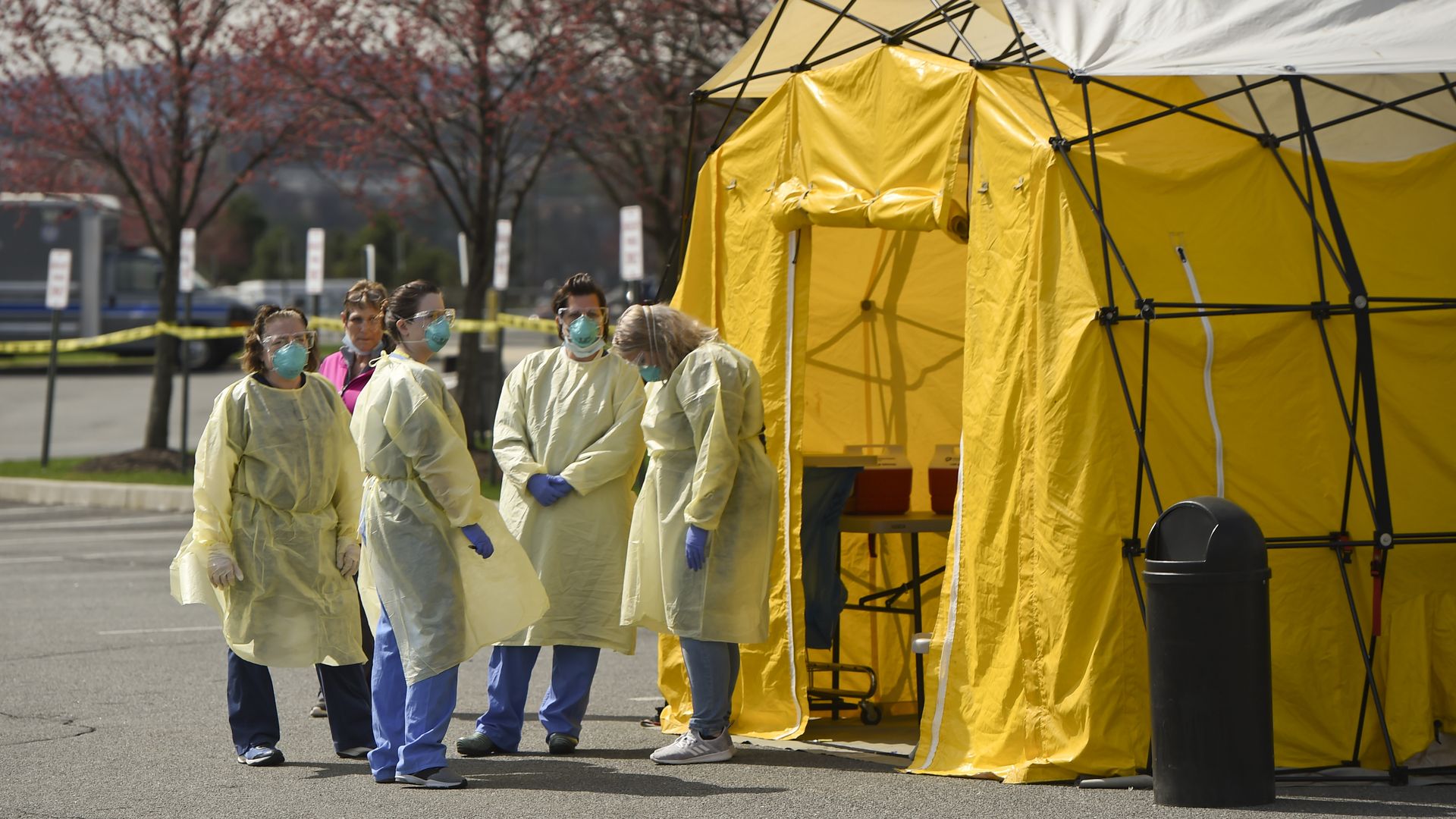 Nurses in masks, goggles, gloves, and protective gowns, wait stand outside the yellow tent 