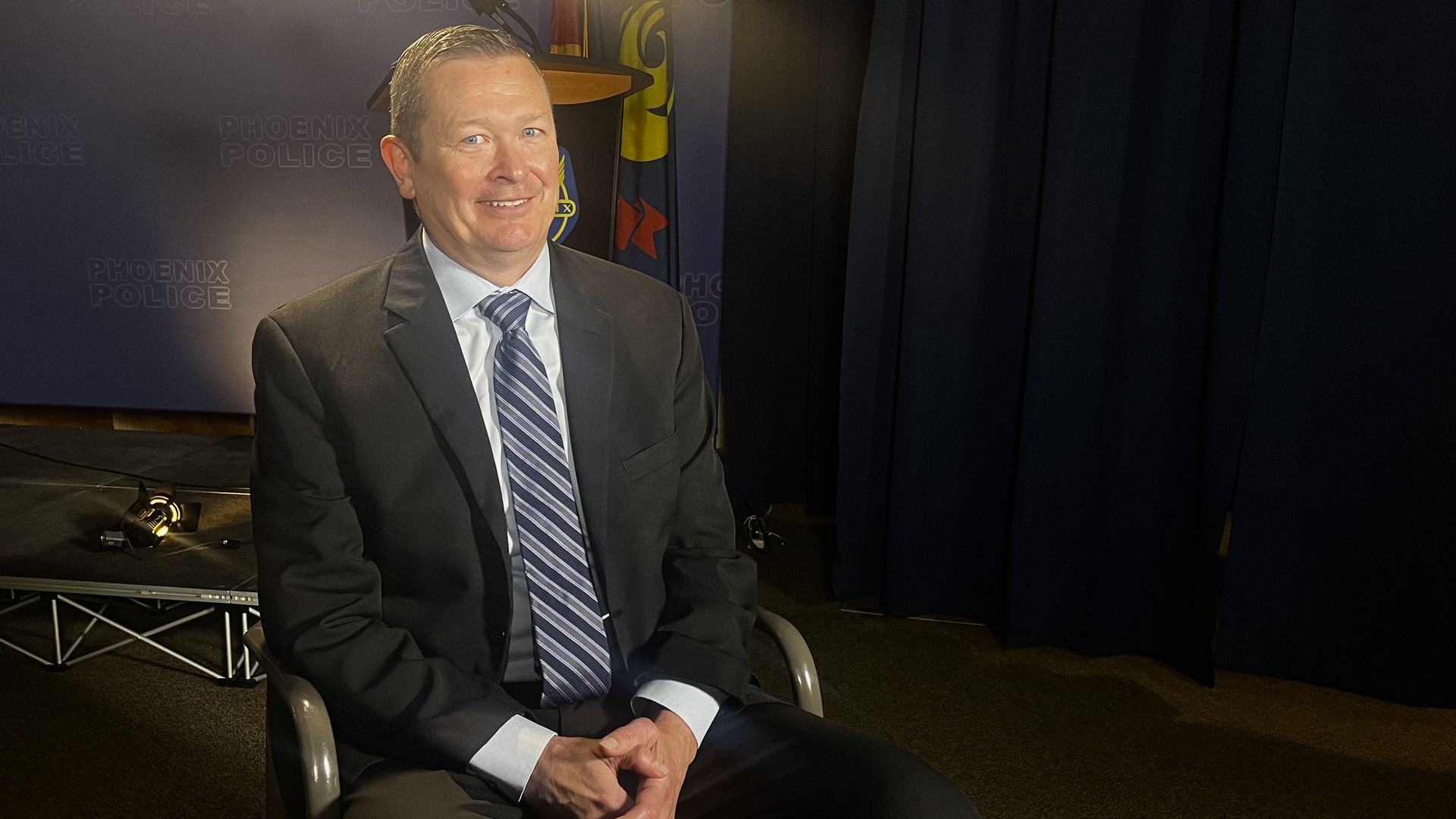 A man in a suit sitting under studio lights.