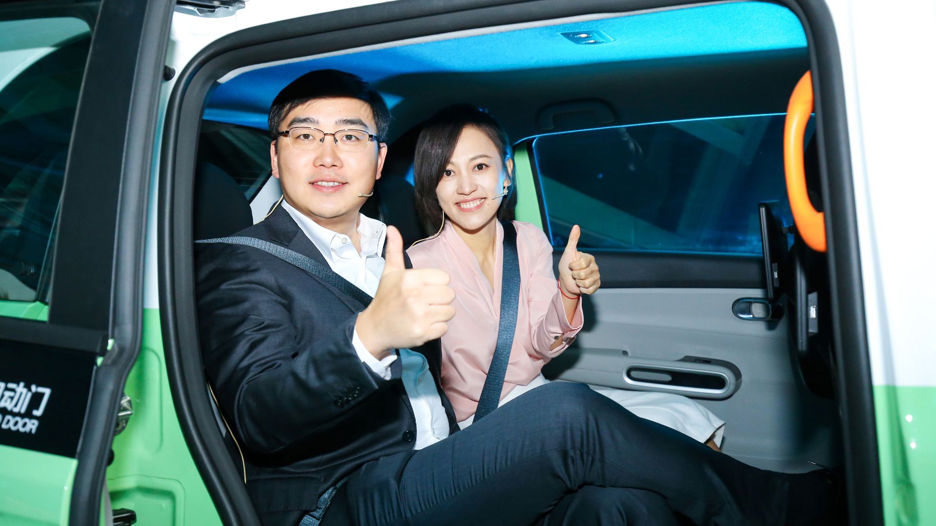Photo of two people sitting in a green car with giving a thumbs-up