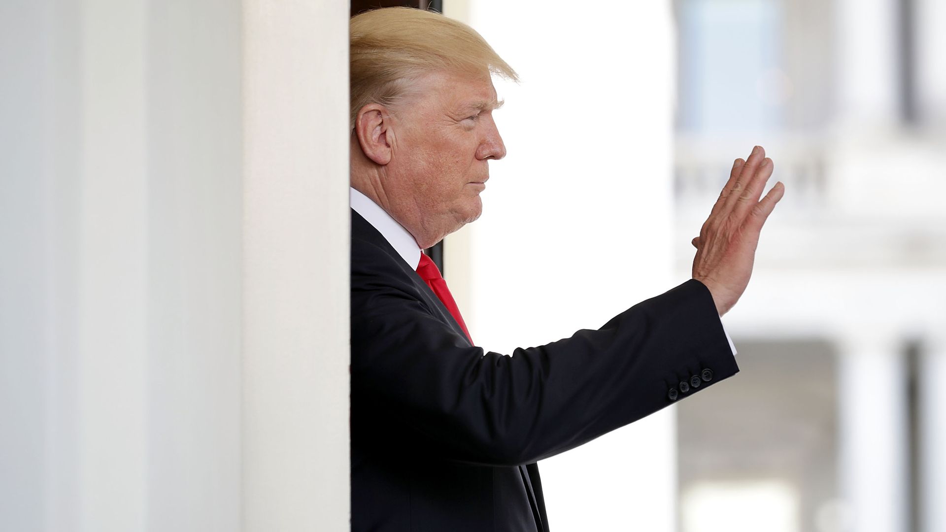 In this image, Trump waves from behind a white pillar. 