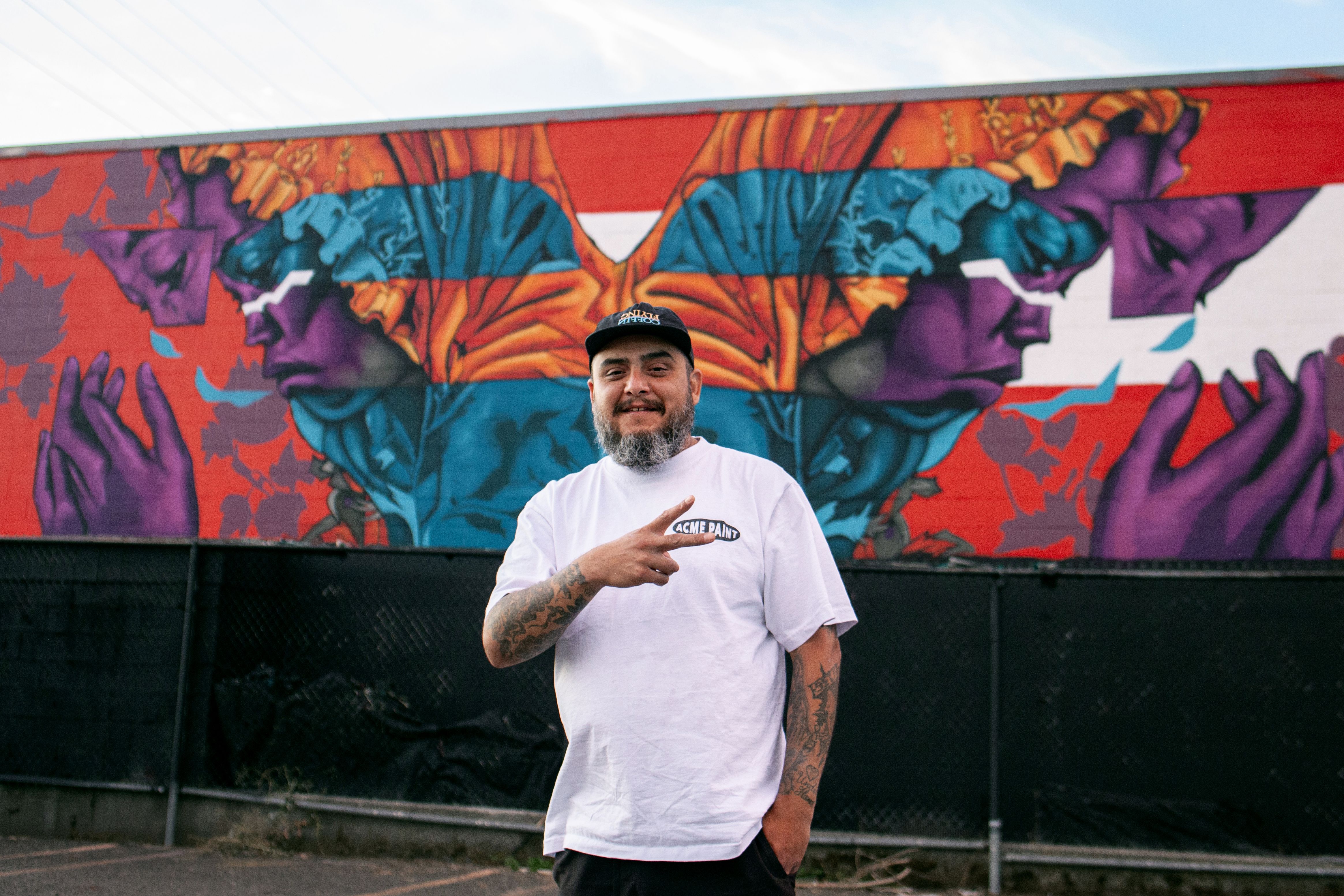 An artist stands in front of a colorful mural in Seattle. 