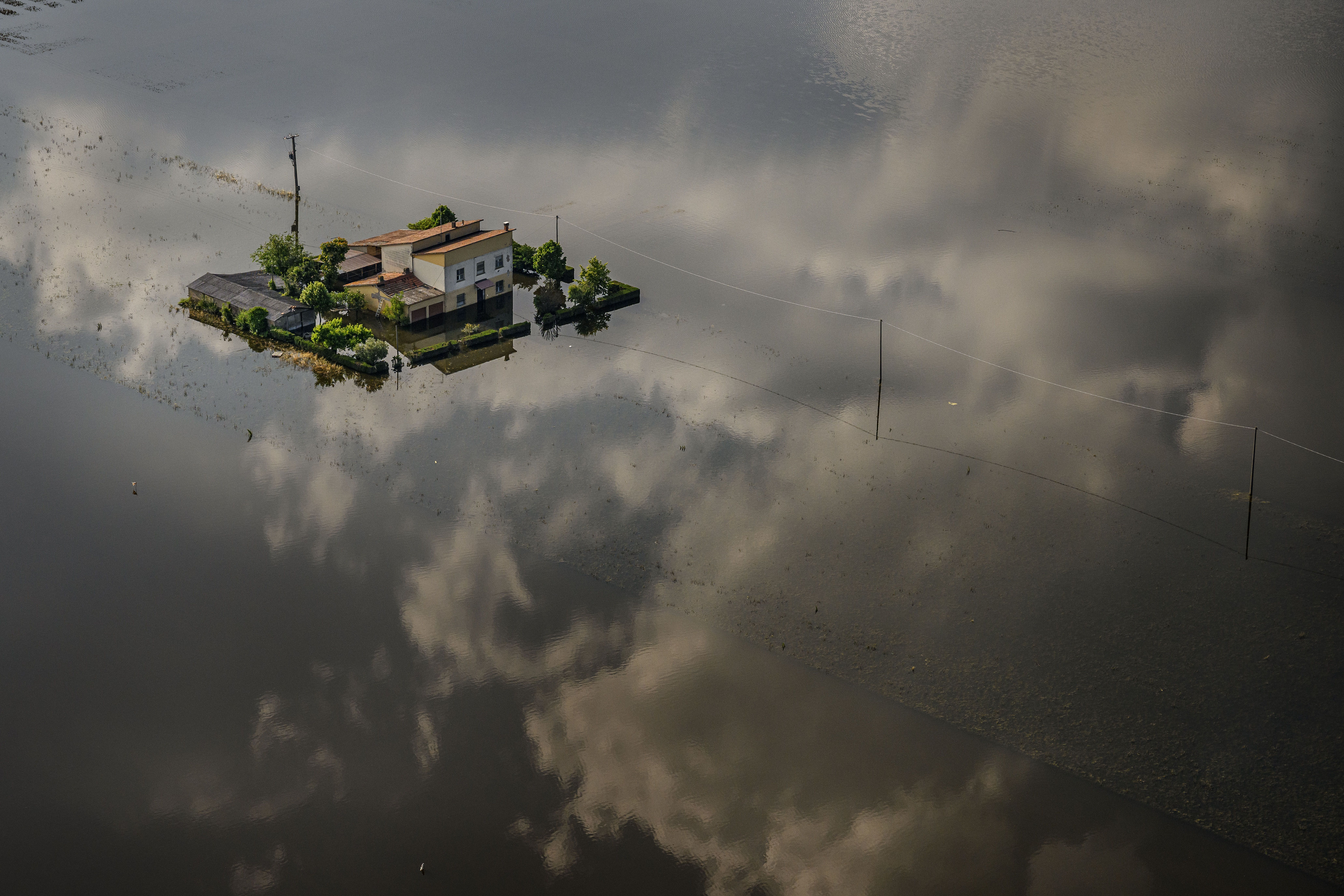 An aerial photograph of a lone house completely surrounded by water. The cloudy sky is reflected in the water surrounding the house. 