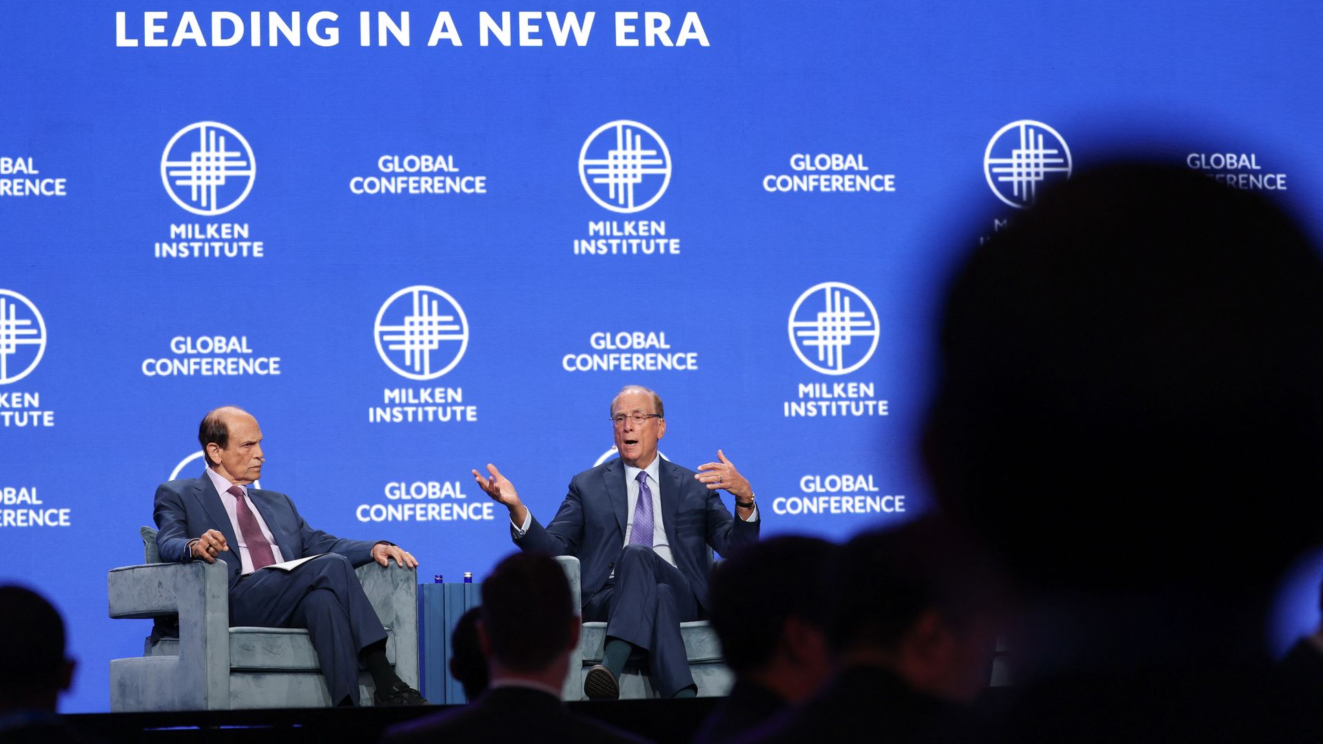 Michael Milken, left, and Larry Fink, right, seated in chairs on stage at the Milken conference.