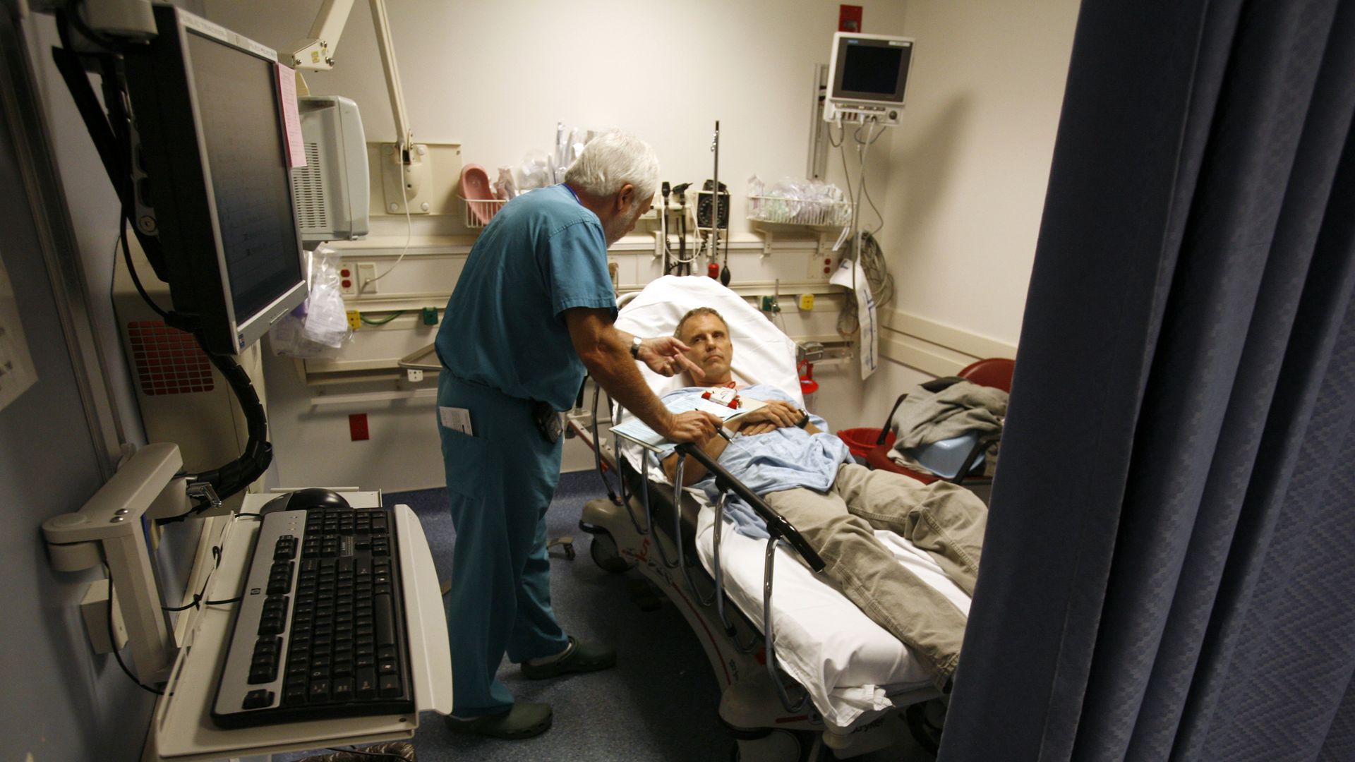 A doctor checks on a patient in an emergency room bed.