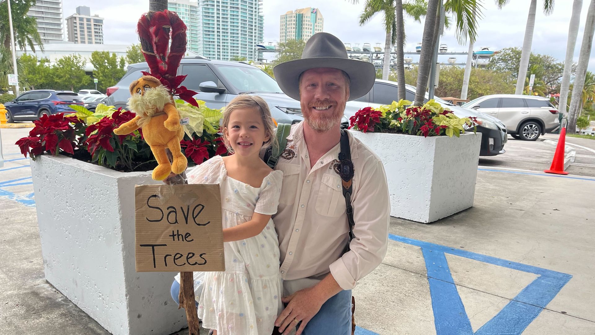 A man and a young woman holding a sign that reads 'Save the Trees.'