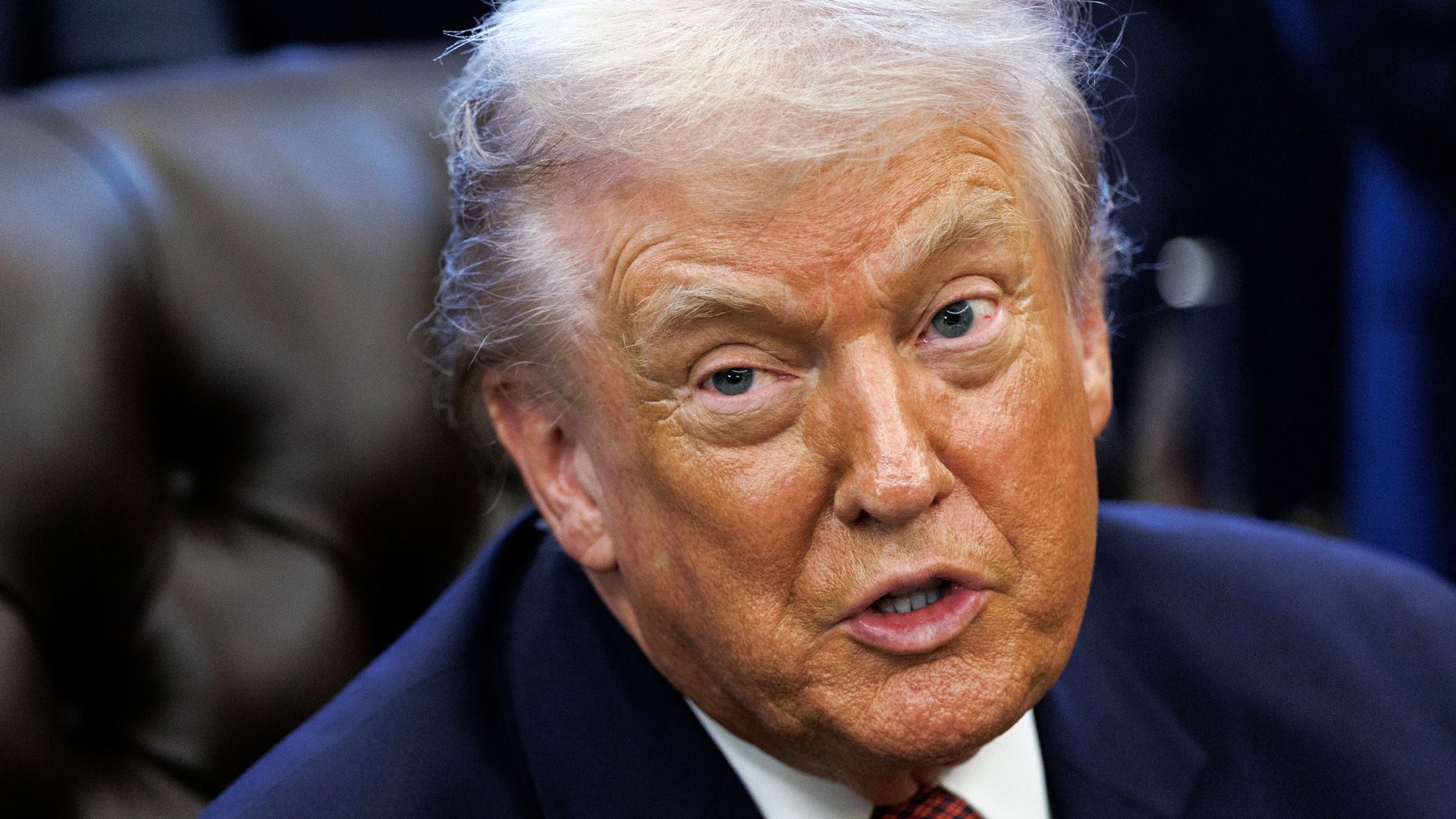 A closeup of President Trump's face as he's seated behind his desk in the Oval Office.