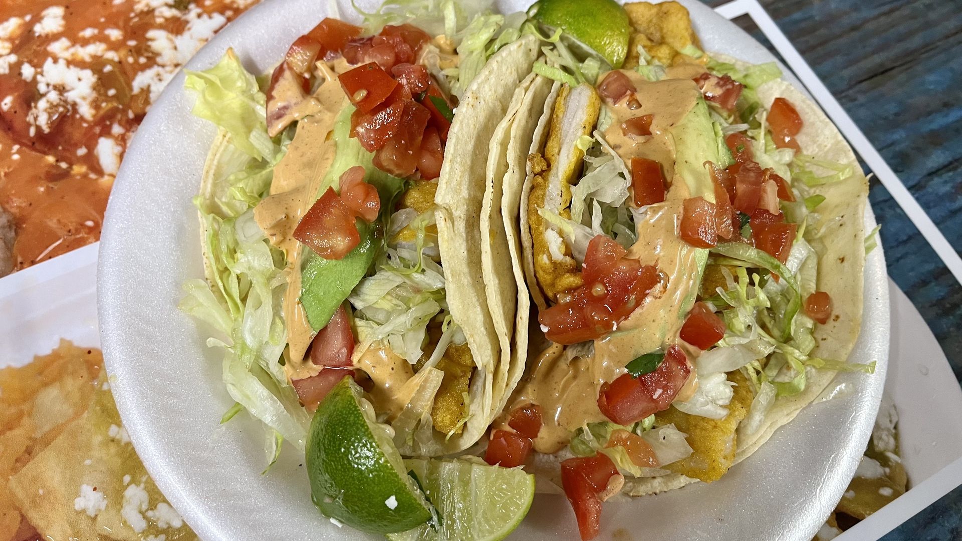 A picture of two loaded fish tacos on a paper plate