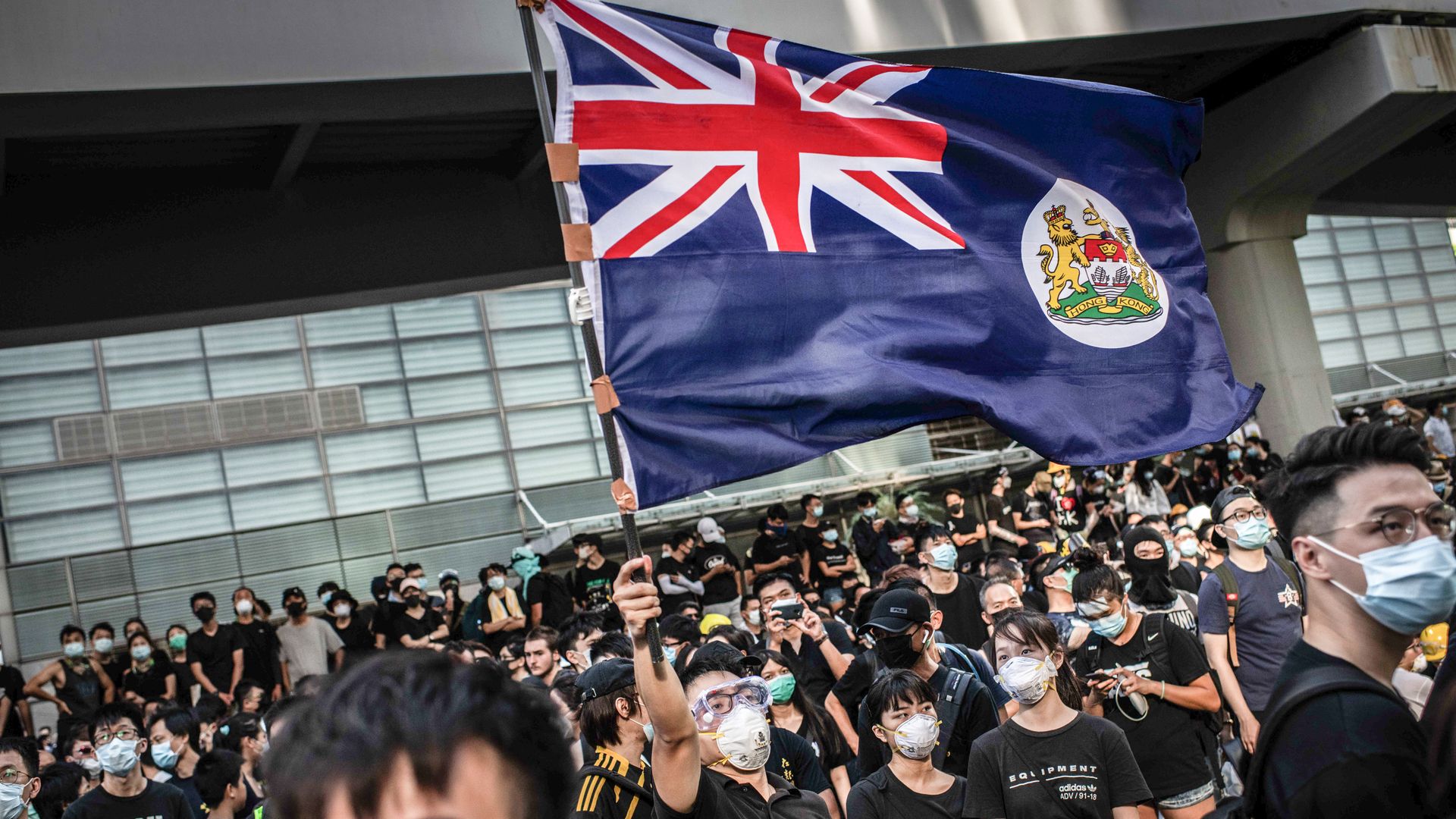 Protester waves Hong Kong colonial flag in the middle of crowd in front of Hong Kong Legislative Council building during demonstration against the extradition law to China.