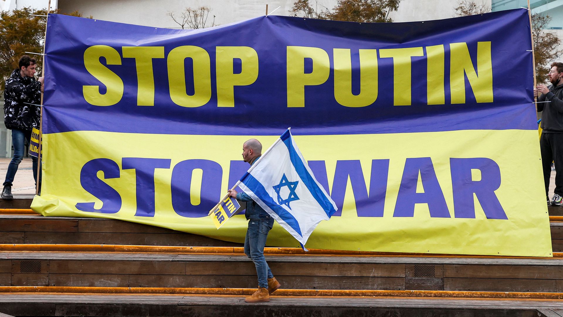 A demonstrator holds up an Israeli flag while standing before an anti-war banner during a protest against Russia's invasion of Ukraine in Tel Aviv.