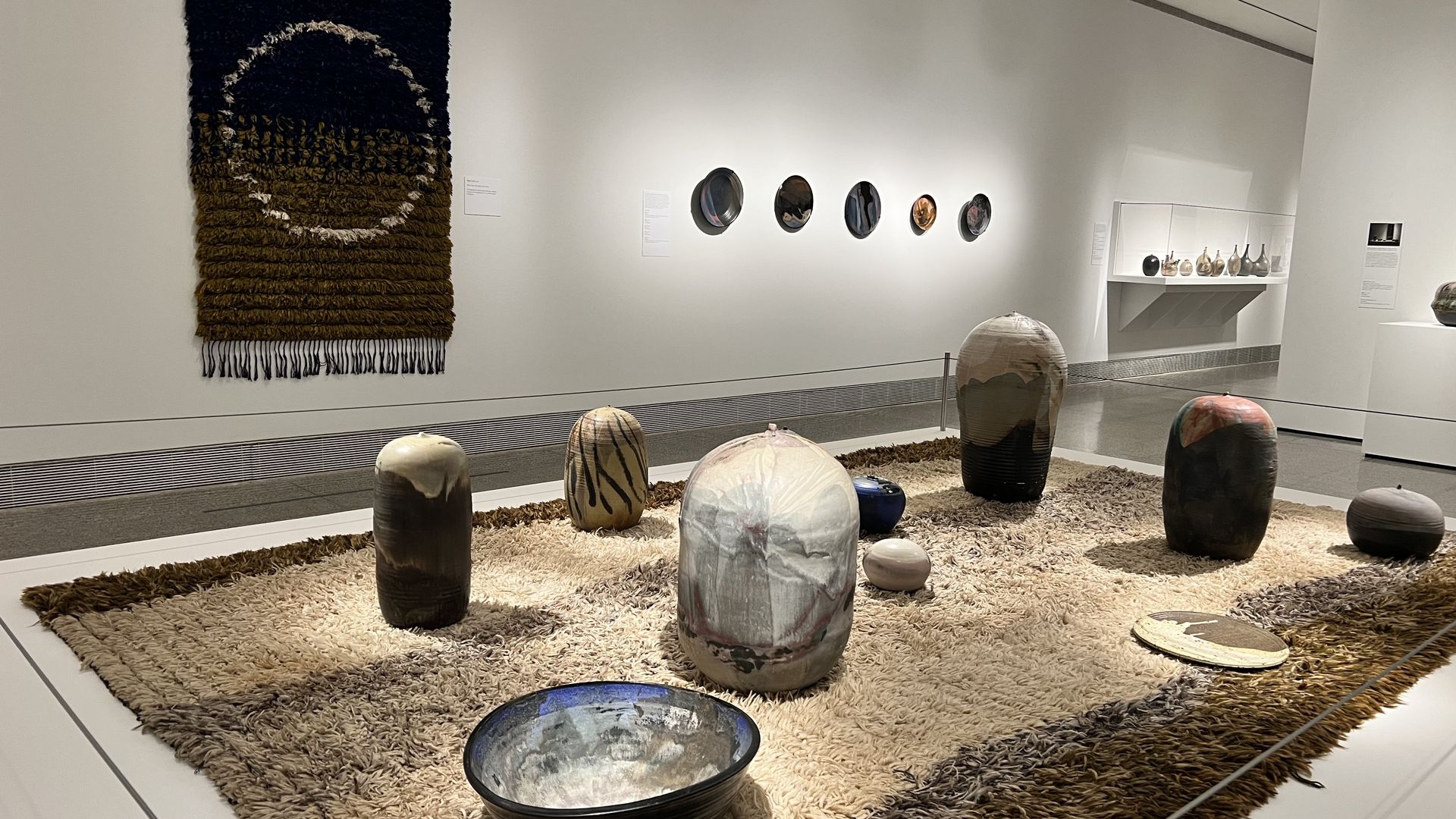 Photo of a group of vessels and sculptural ceramic pieces on a rug. 