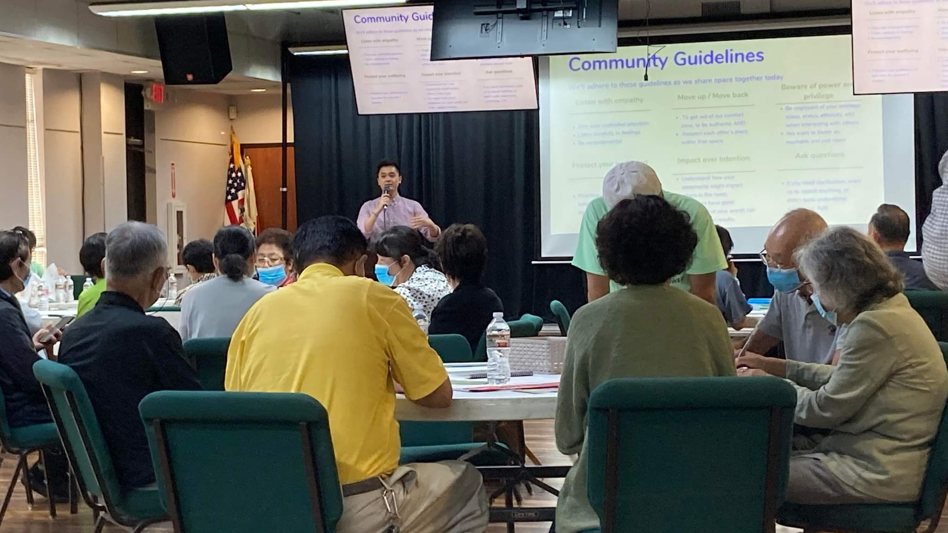 A group of Asian Americans sitting in groups during a presentation. 