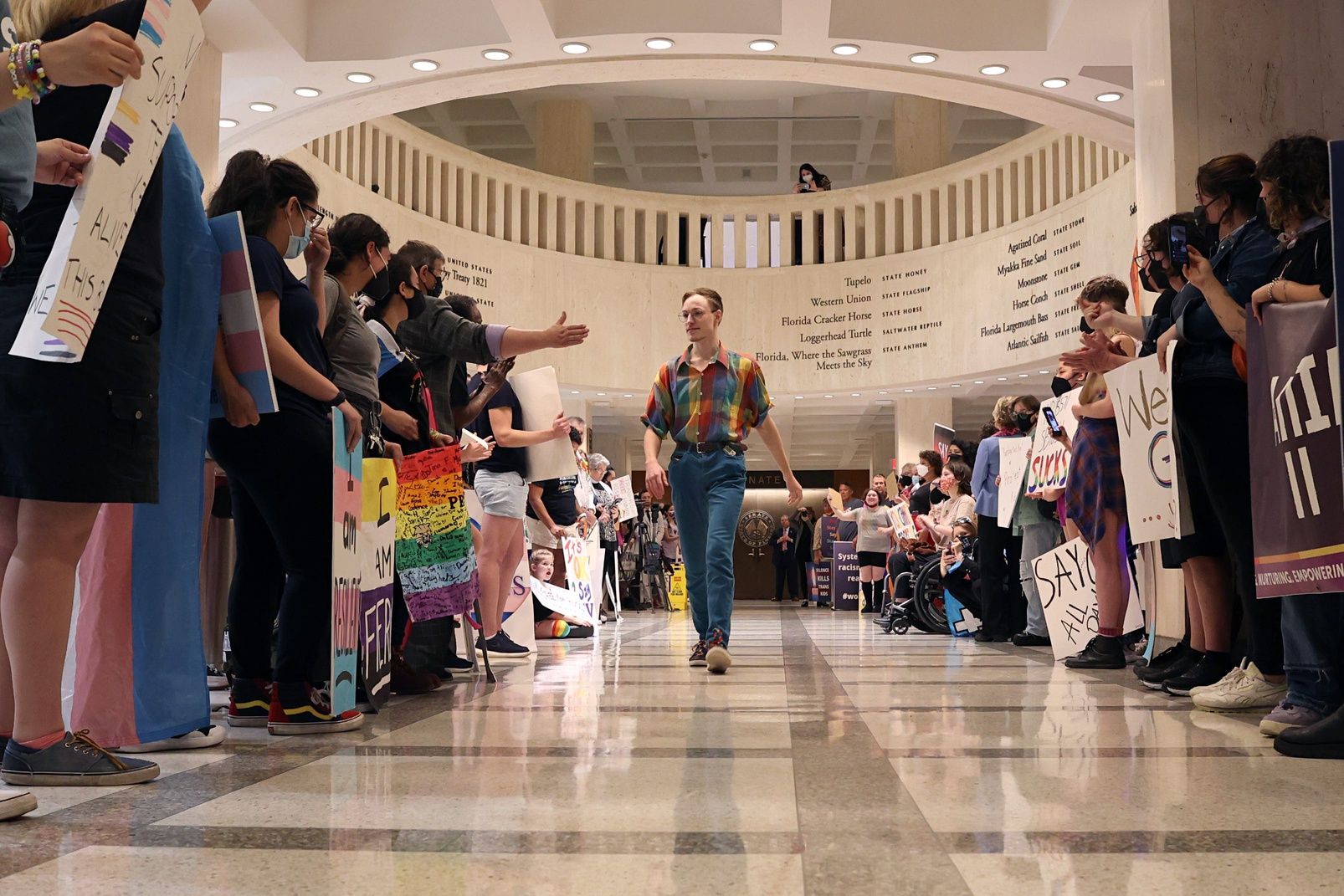 a person walks down the center of a group of LGBTQ protesters in the senate