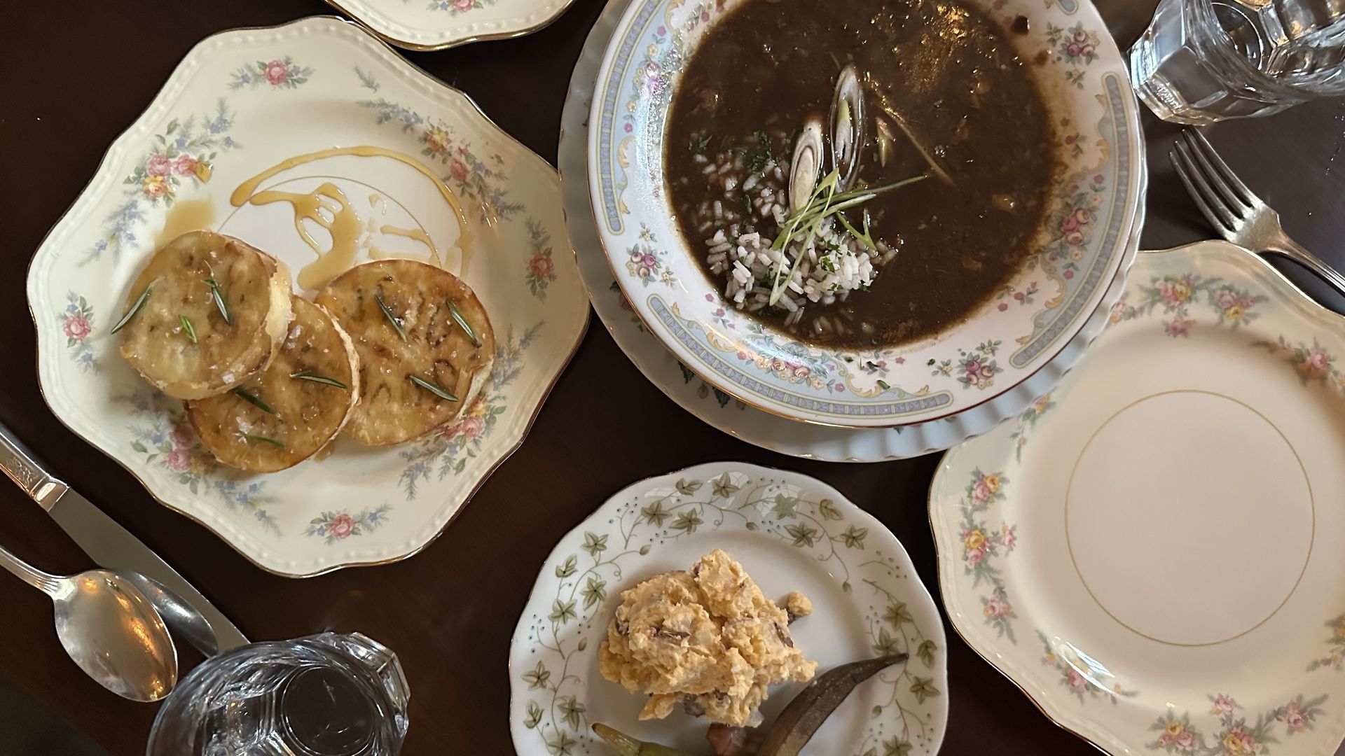 A wooden table is set with gumbo, potato salad and fried eggplant.