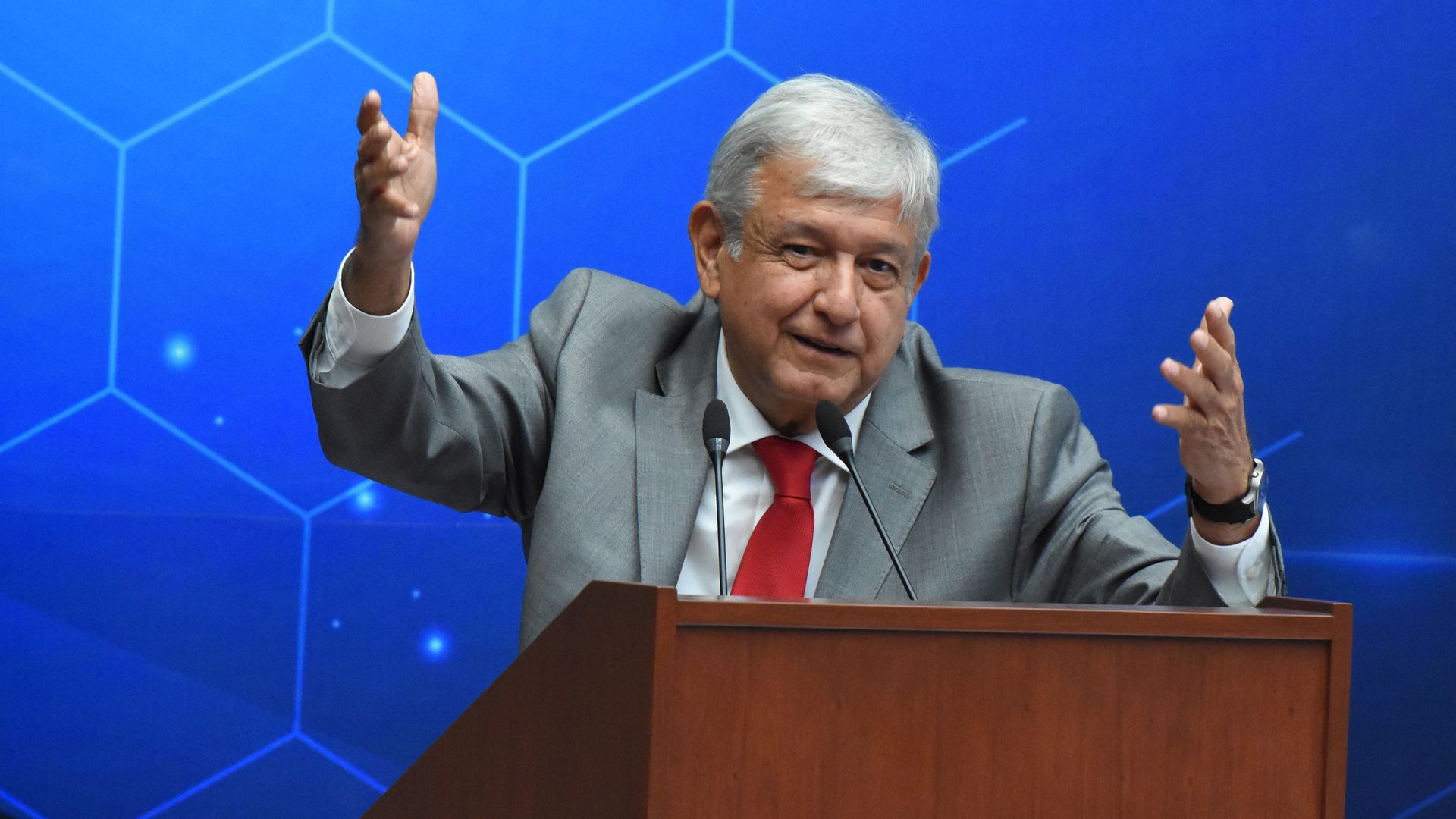 Andres Manuel Lopez Obrador speaking at a lectern with arms raised in gesture