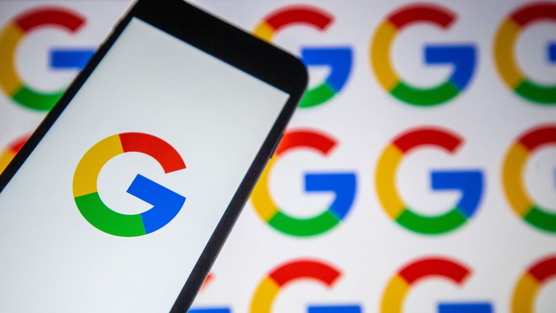 A photo of a smartphone with a Google logo on the screen over images of the Google logo.