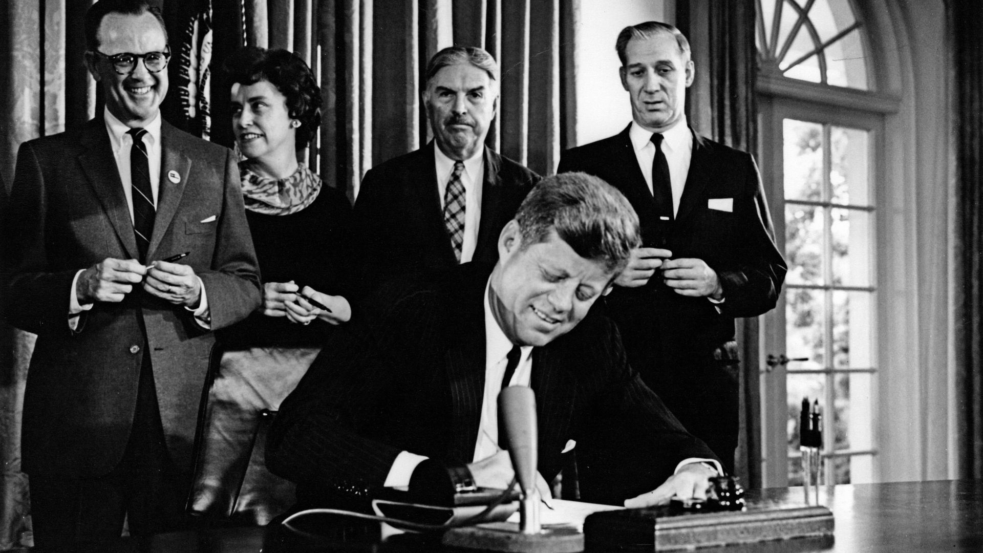 President John F. Kennedy signs Detroit's bid to host the 1968 summer Olympics, with Michigan officials behind him. 