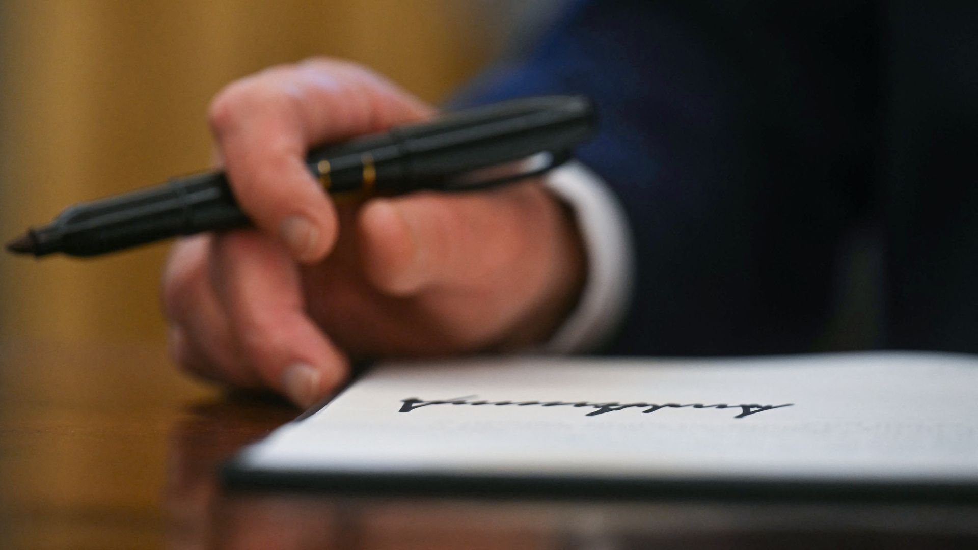 A zoomed in photo of Trump's hand holding a marker. His signature is written on a paper below his hand.