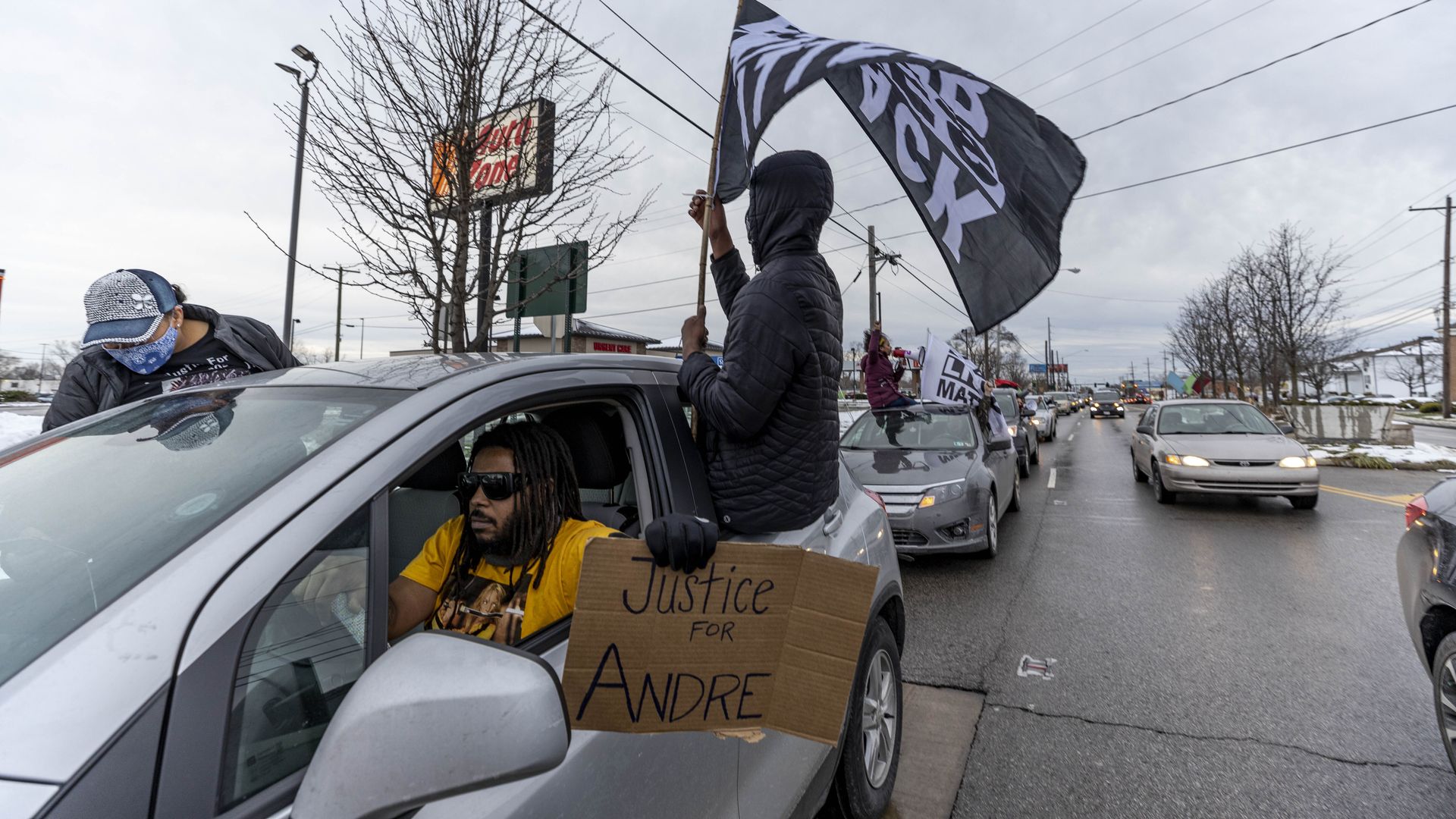 Photo of people in a car waving signs and banners demanding justice for Andre Hill