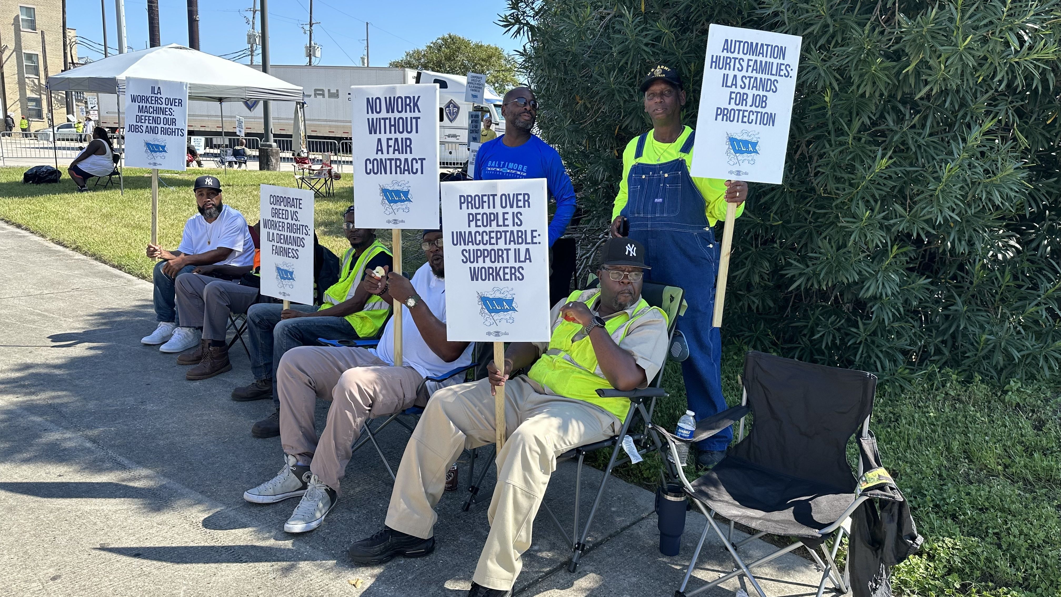About 8 men stand near a roadway with picket signs.