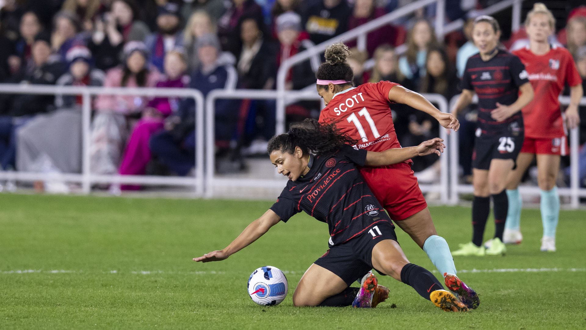 four women in soccer uniforms around a soccer ball on the field