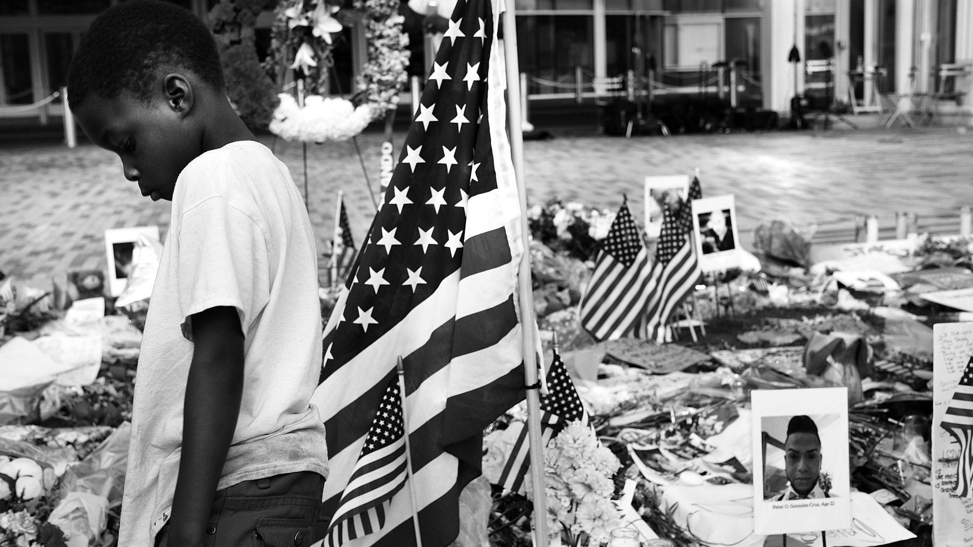 A vigil for victims of the Pulse nightclub shooting in Orlando with boy standing in front of memorial.