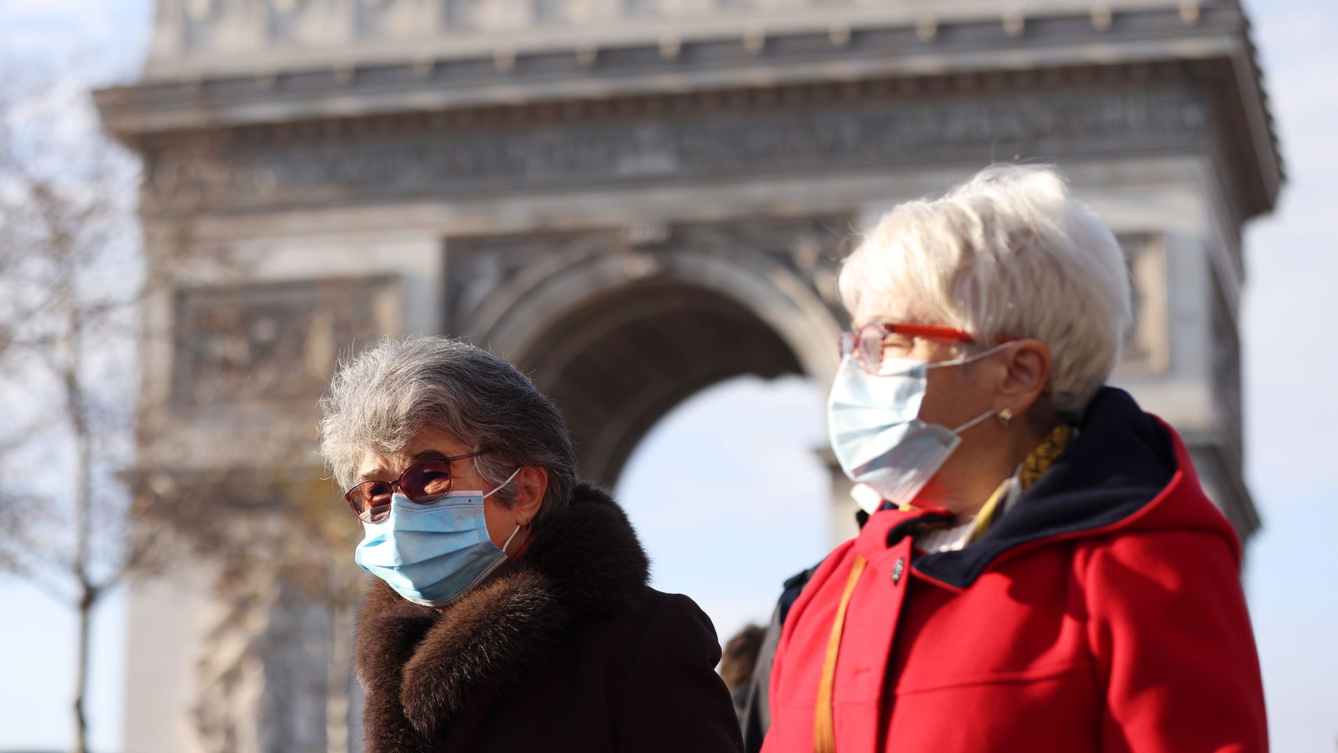 People wearing face masks walk near the Arc de Triomphe in Paris
