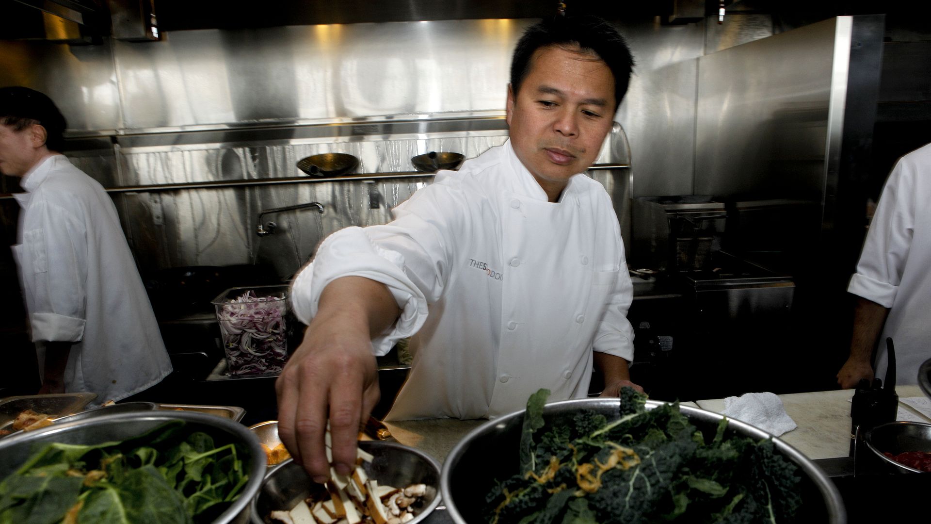 Photo of Charles Phan working in a kitchen while grabbing ingredients from metal bowls