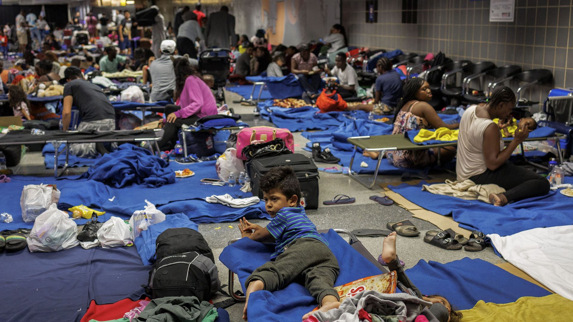Recently arrived migrants sit on cots and the floor of a makeshift shelter operated by the city at O'Hare International Airport.