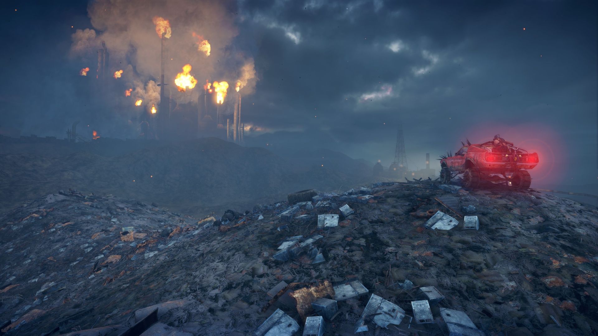Vide game screenshot of a car parked on a junk heap underneath a dark sky, a factory's towers burning off flame in the distance