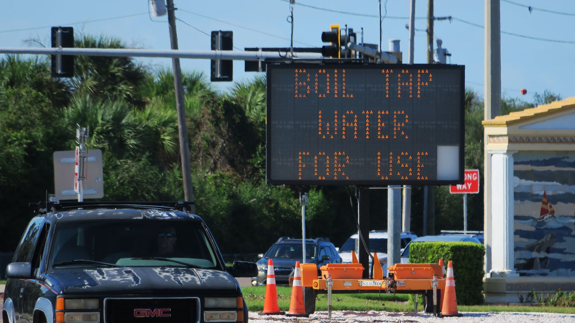 A black sign on the side of the road that reads, "BOIL TAP WATER FOR US" in orange letters.