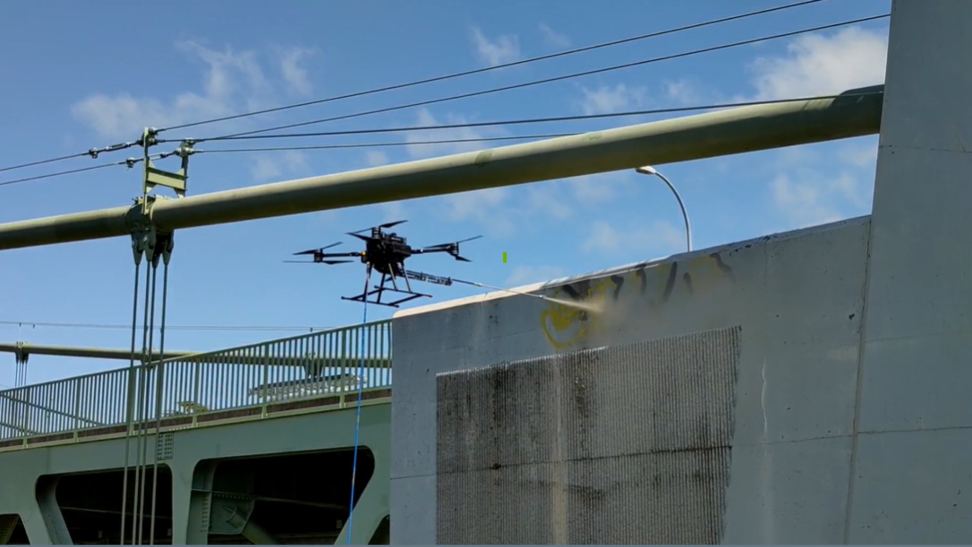 A hovering drone sprays paint over graffiti tags along a freeway wall.
