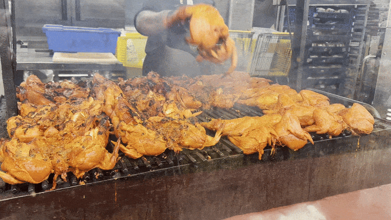 Image shows chicken being cooked on the grill with a person flipping the meat.