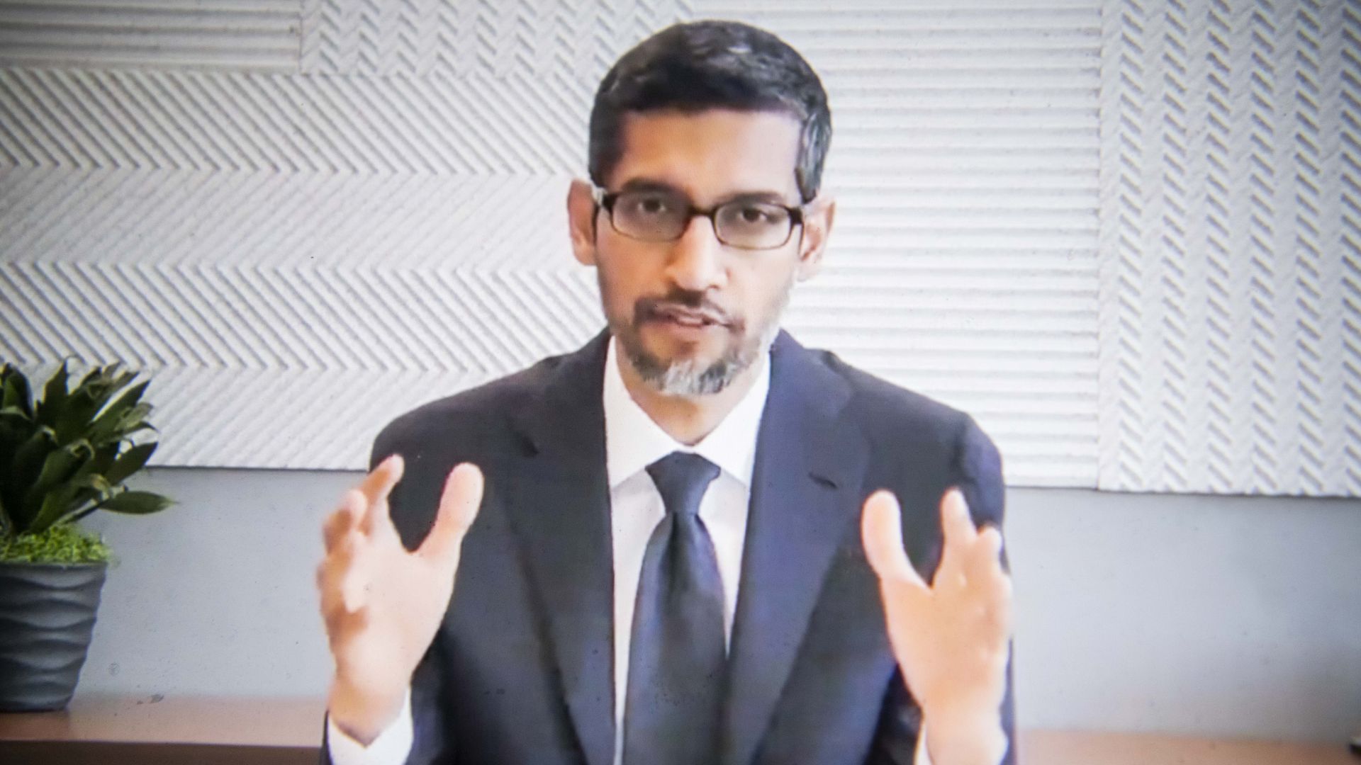 Photo of Google CEO Sundar Pichai in a suit at a desk speaking in a videoconference