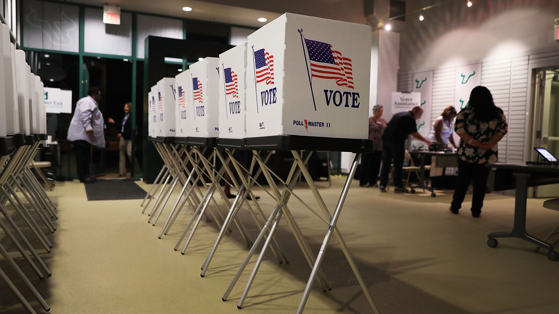 In this image, a row of voting booths are seen in a room with darkened windows.