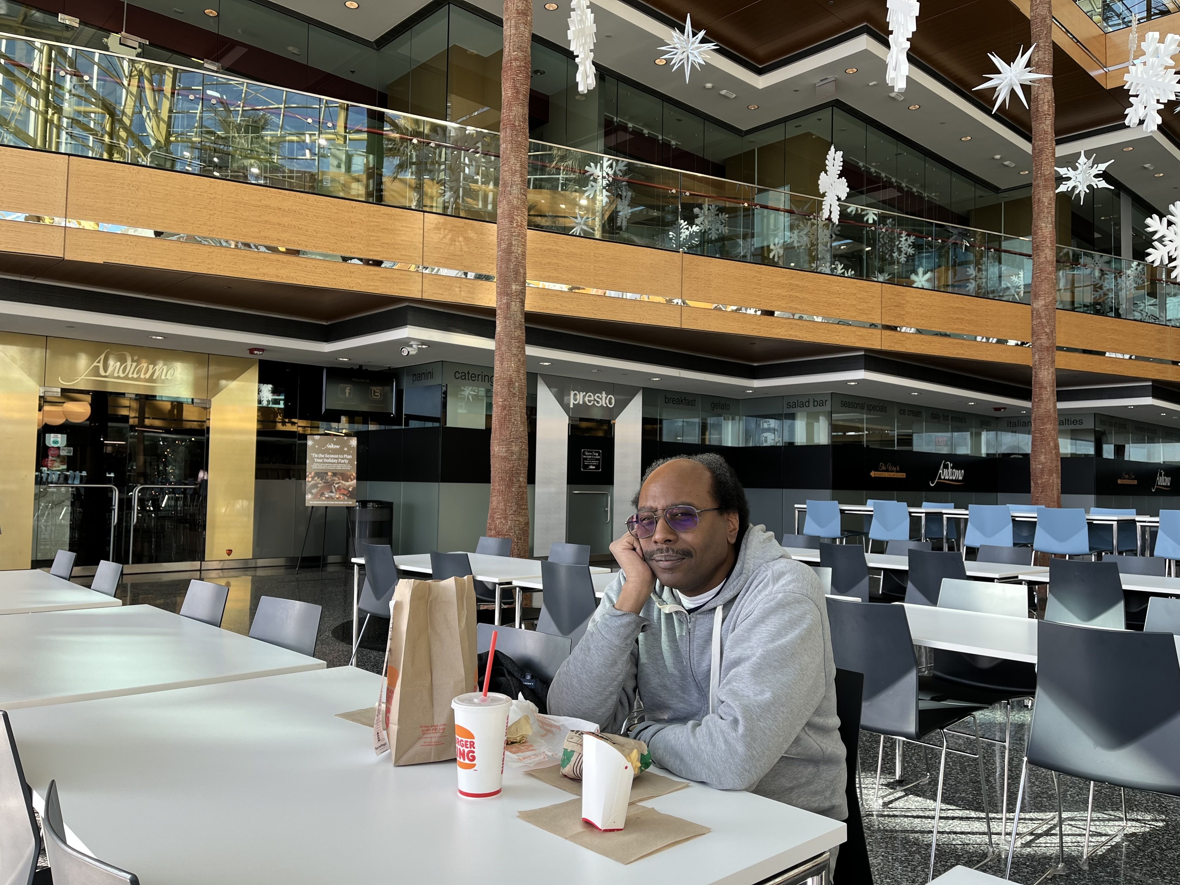 The man sits with his lunch in the atrium, posing with a slight smile. 